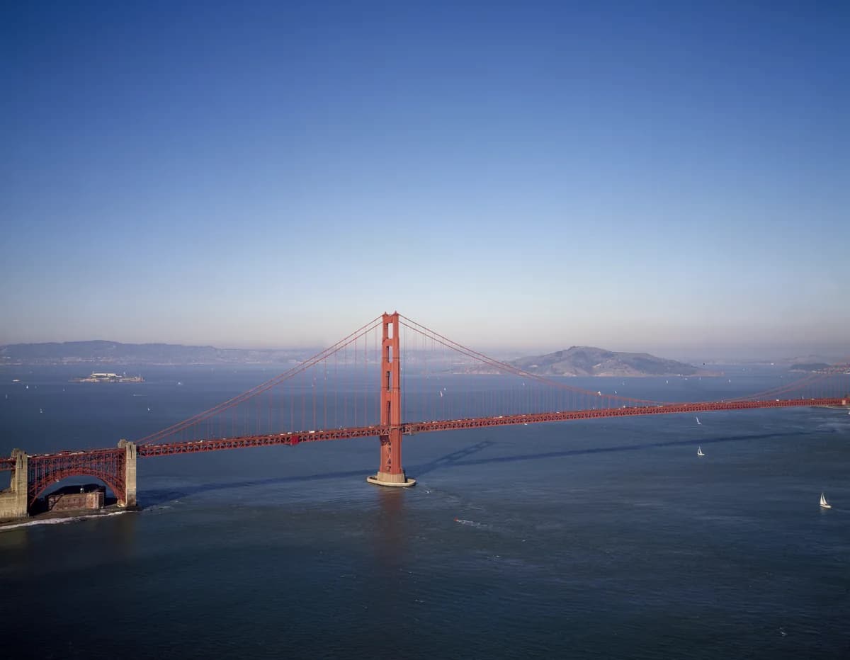 The Golden Gate Bridge, painted orange red, crossing the bay under a clear blue sky