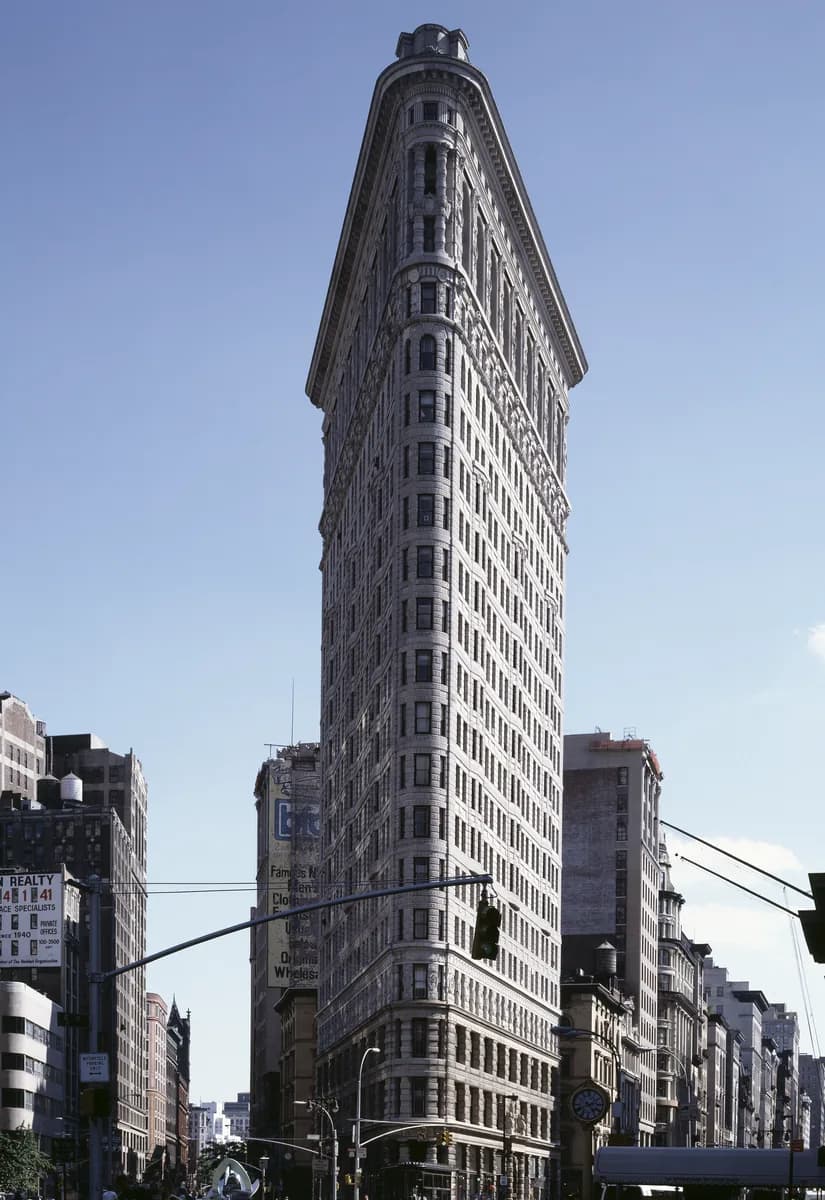 The narrow, wedge shaped Flatiron Building rising above Manhattan streets under a blue sky