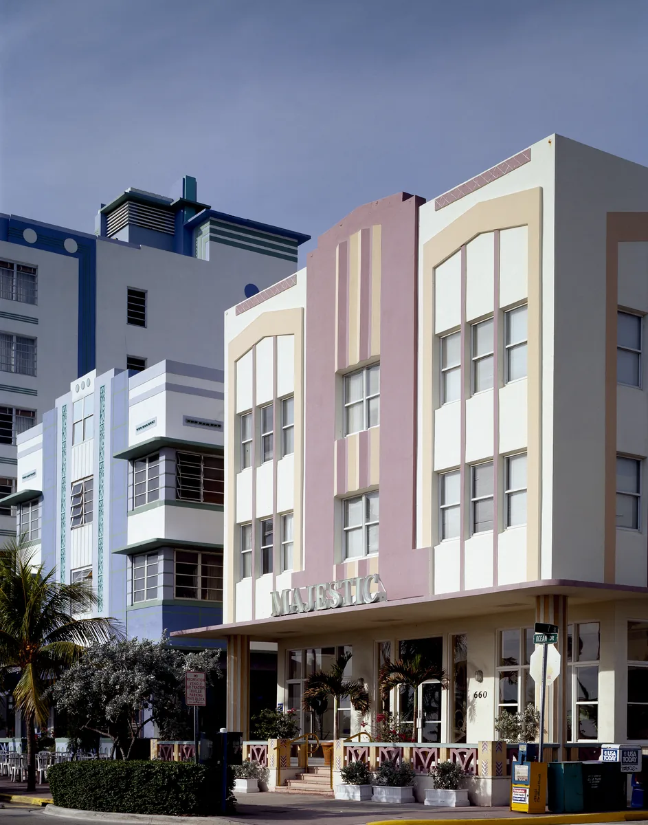 Pastel Art Deco hotels on a Miami Beach street corner, with the word MAJESTIC on the entrance canopy, palm trees and a blue sky
